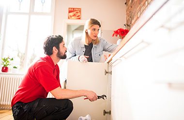 HomeServe approved plumber fixing pipe under sink, with customer 